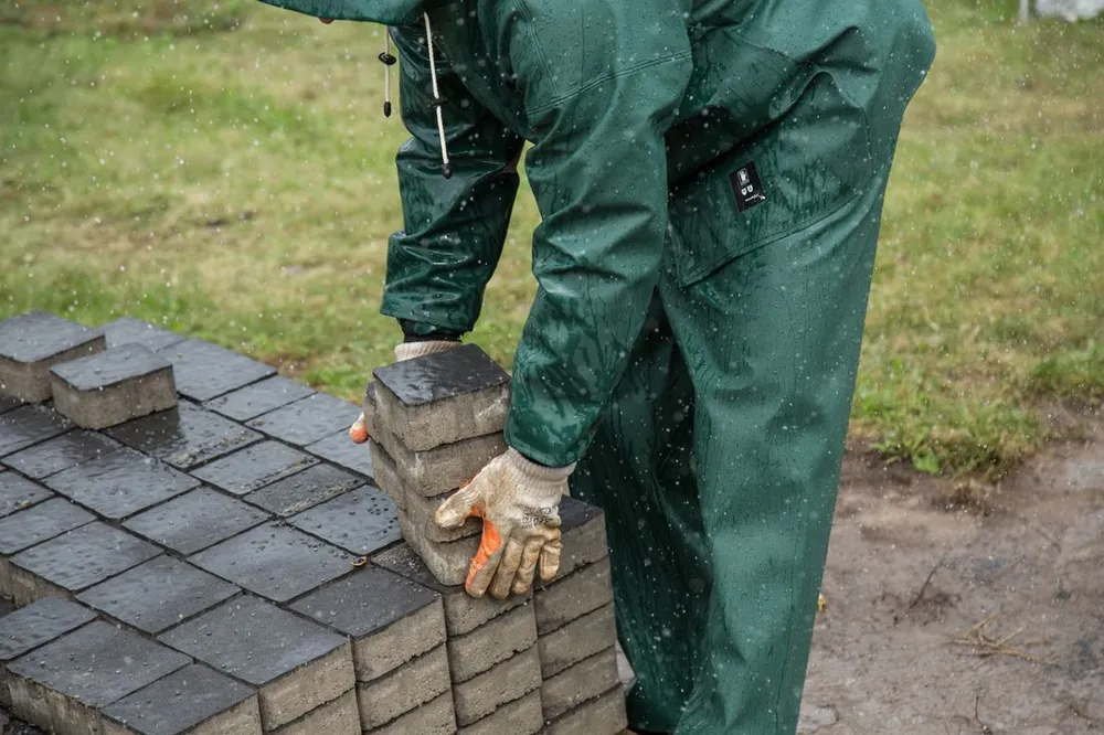 Handwerker mit Arbeitshandschuhen beim Vorbereiten von Pflastersteinen im Außenbereich – Symbolbild